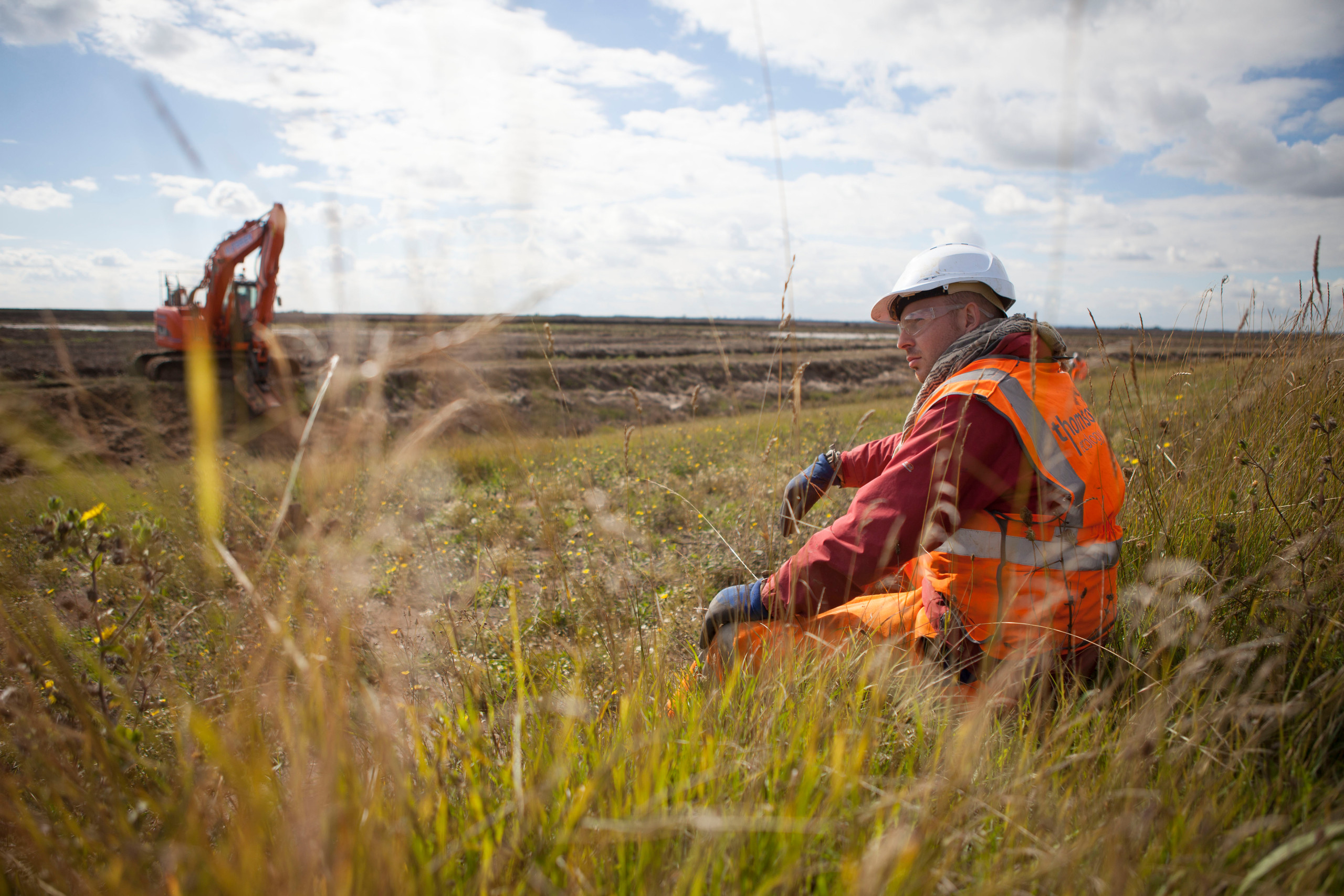 Photo of worker sitting in grass at Wallasea Island with an excavator in the background